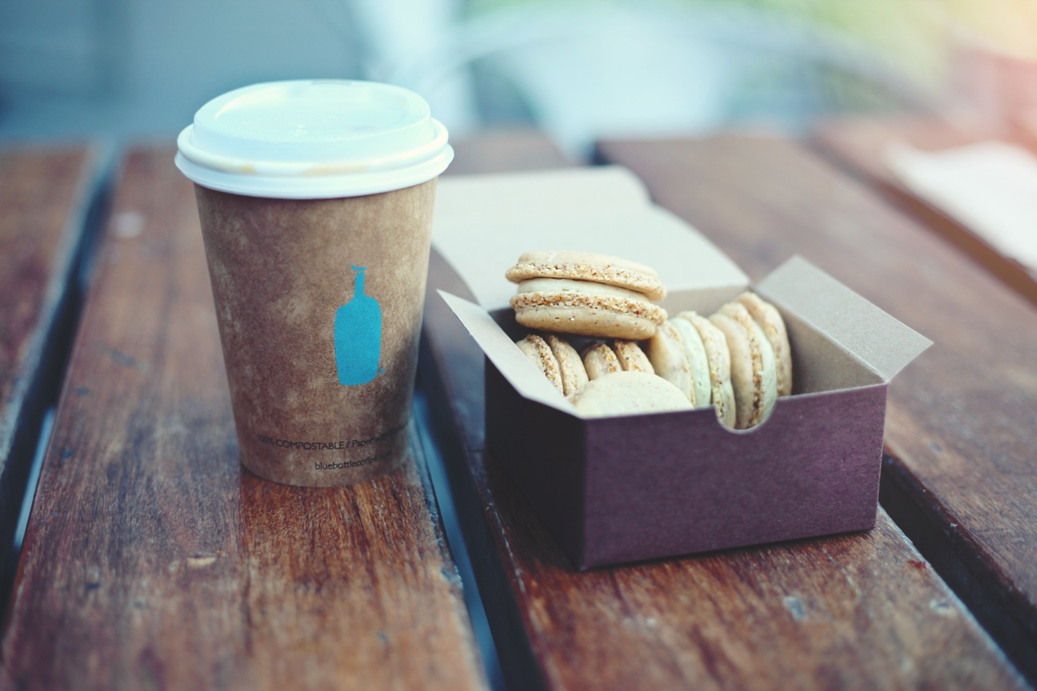 A take away coffee in a compostable cup with an open box of cookies on a wooden bench