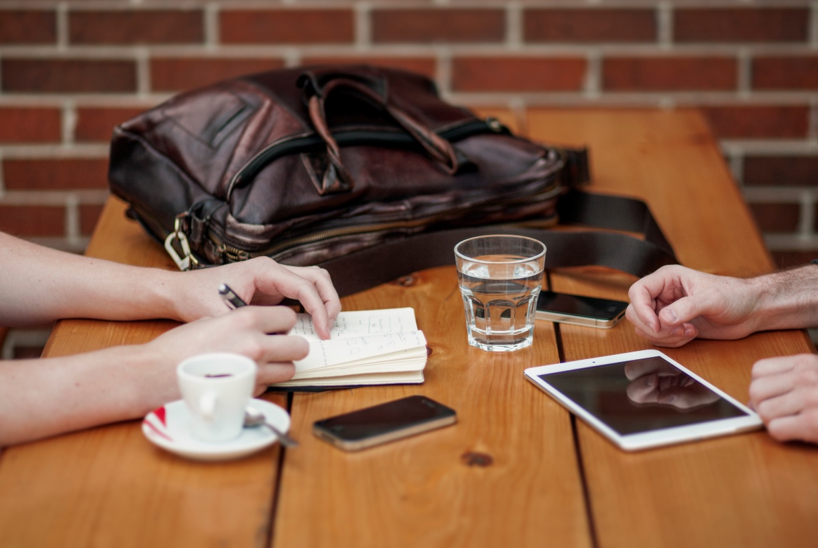 Photo of hands on a wooden table with a glass of water between an iPad and mobile device.