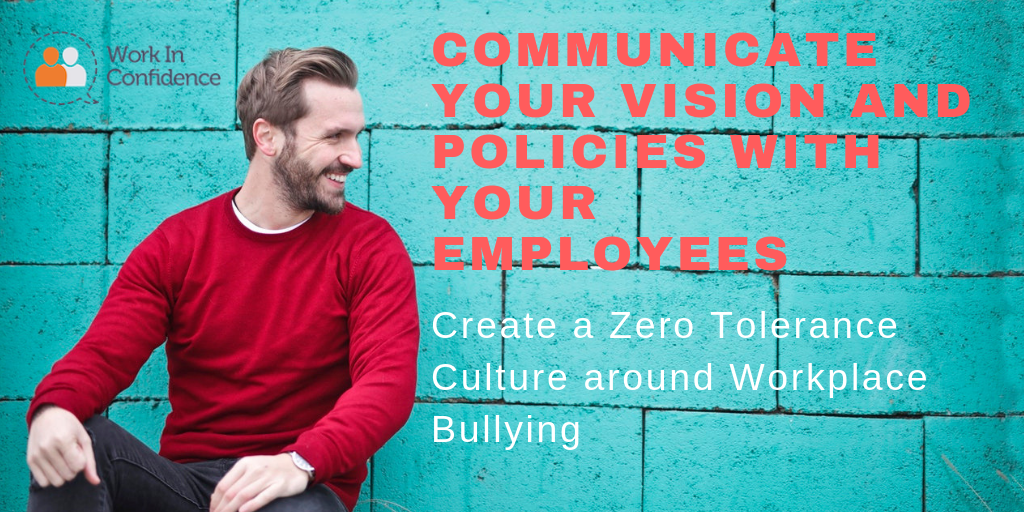 A photo of a man sitting by a teal wall wearing a red jumper smiling with the text "Communicate your vision and policies with your employees - create a zero tolerance culture around workplace bullying"