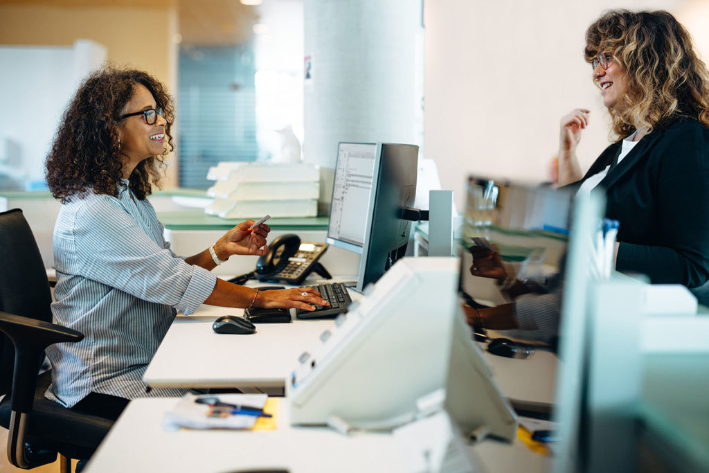 Municipal office administrator assisting a woman standing at her desk. Friendly receptionist helping a woman visiting municipality office.